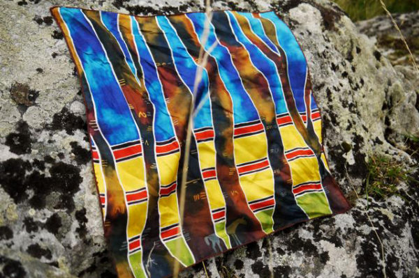 A silk scarf with tree trunks on a yellow and blue background rests on a rock