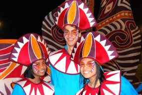 Three performers wear large silk costume with red, brown and yellow spiky pattern