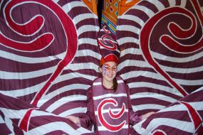 Performer wears large silk costume with red and brown swirly pattern