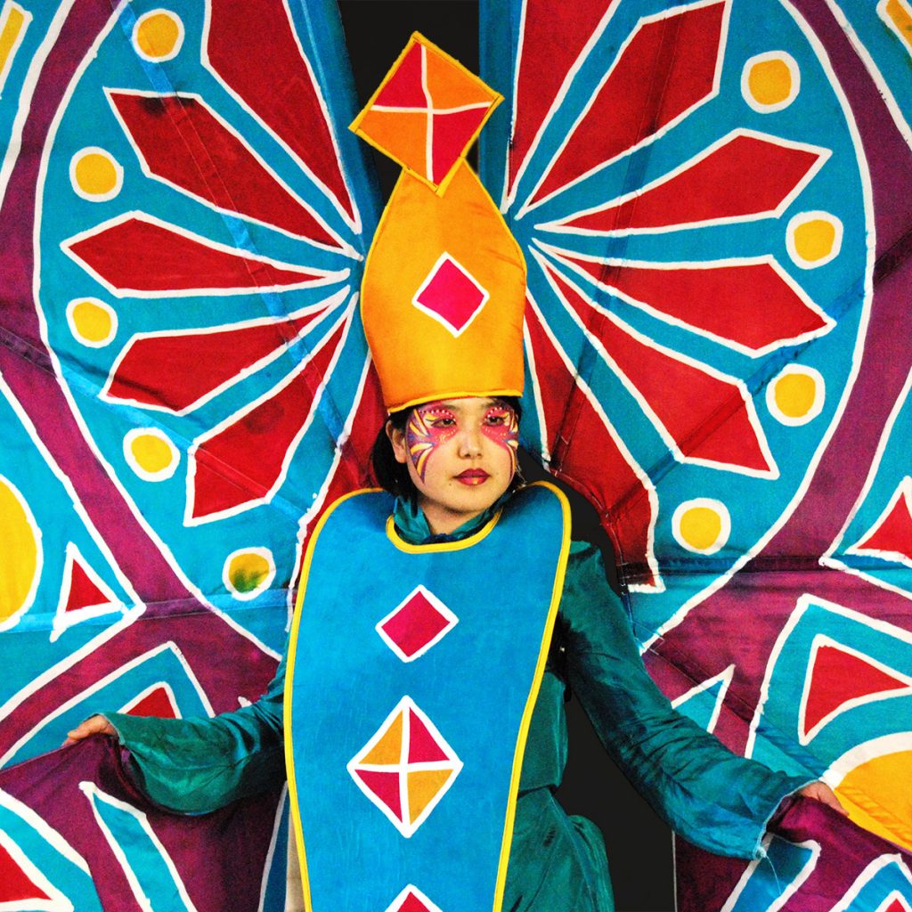 Performer wears large silk carnival costume with stained glass pattern