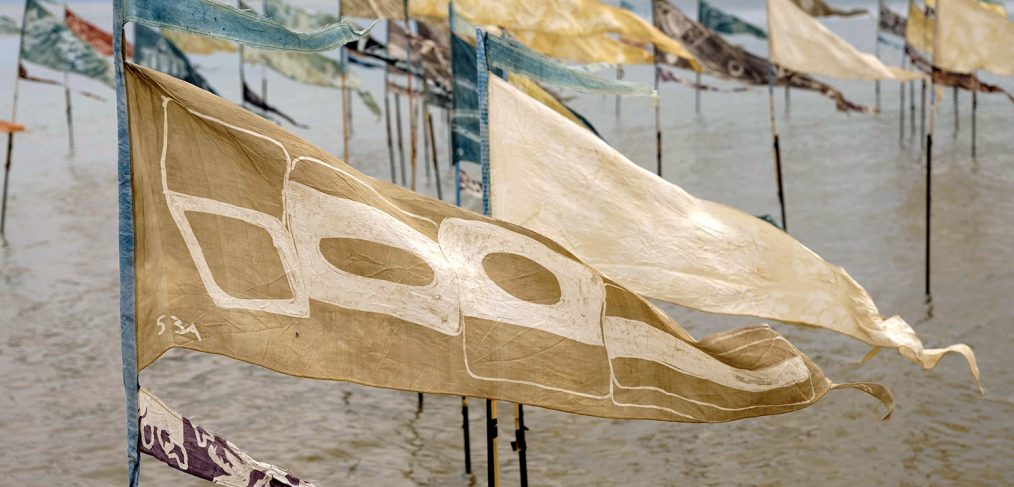 Flags on a beach, held by poles in the sand with the tide coming in