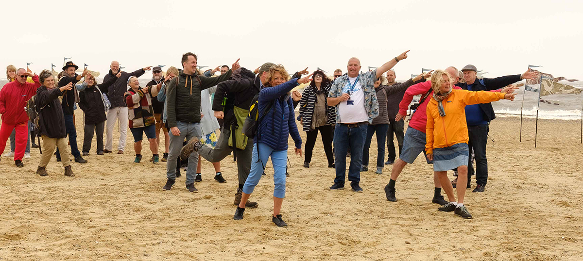 Crowd of Beach of Dreams walkers on Lowestoft beach pointing towards the walk route